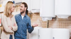 panoramic shot of smiling boyfriend and girlfriend talking near boilers in home appliance store